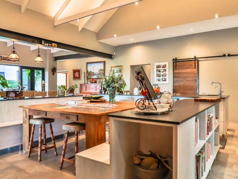 Spacious open-plan living and kitchen area featuring vaulted ceilings, exposed structural beams, modern sliding barn doors, and a large central island with stone countertops.