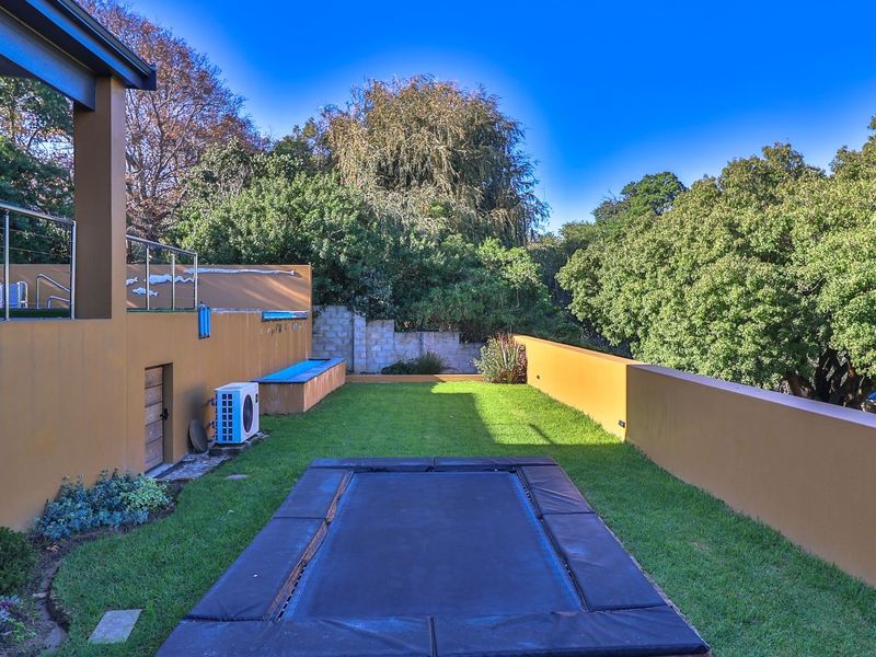 A well-maintained rear garden featuring a lawn, retaining walls, and an elevated patio area with stainless steel balustrades.