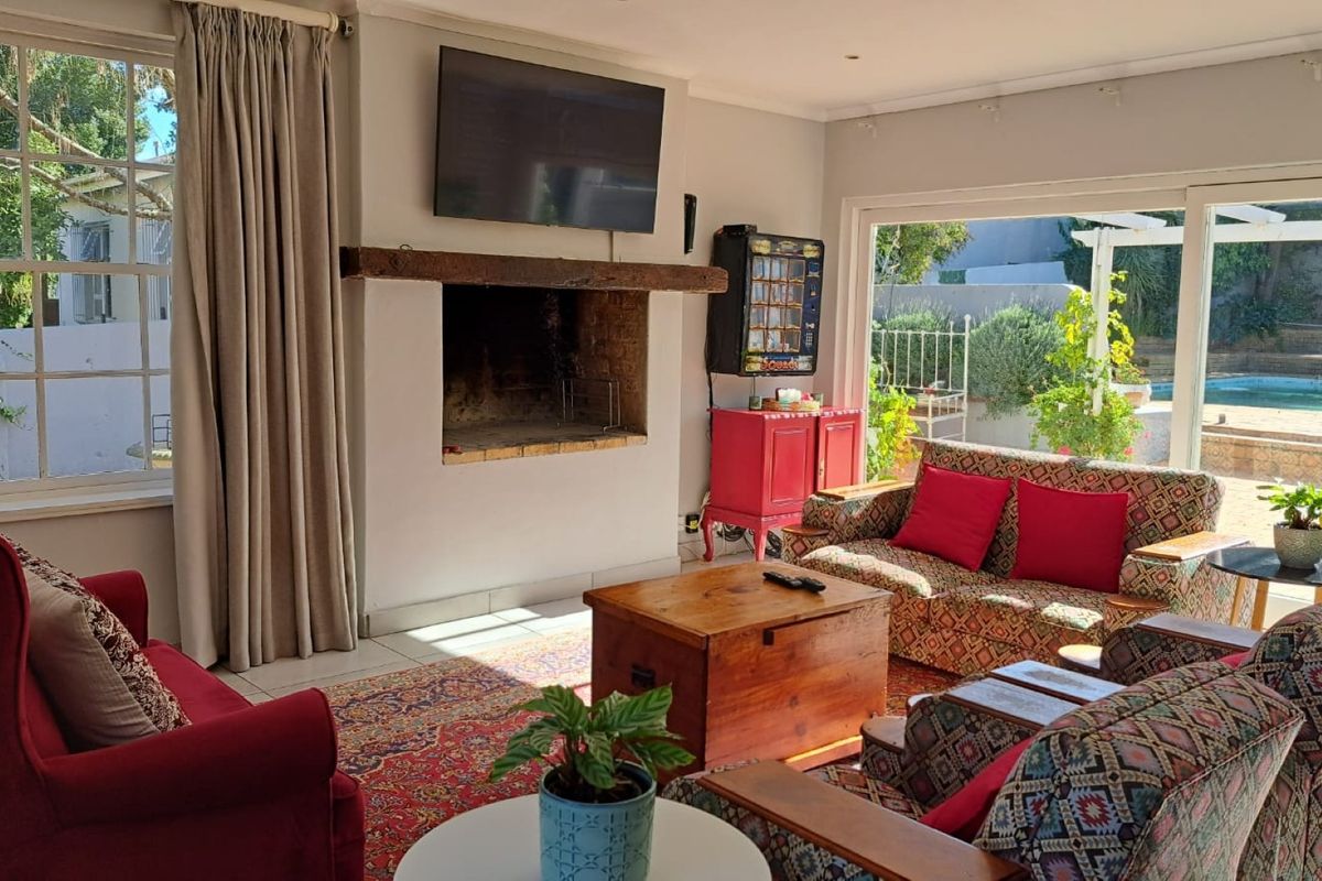 Spacious living room featuring a masonry fireplace with a timber mantelpiece, tiled flooring, and large sliding glass doors opening to the pool area.