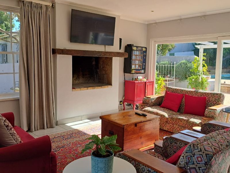 Spacious living room featuring a masonry fireplace with a timber mantelpiece, tiled flooring, and large sliding glass doors opening to the pool area.