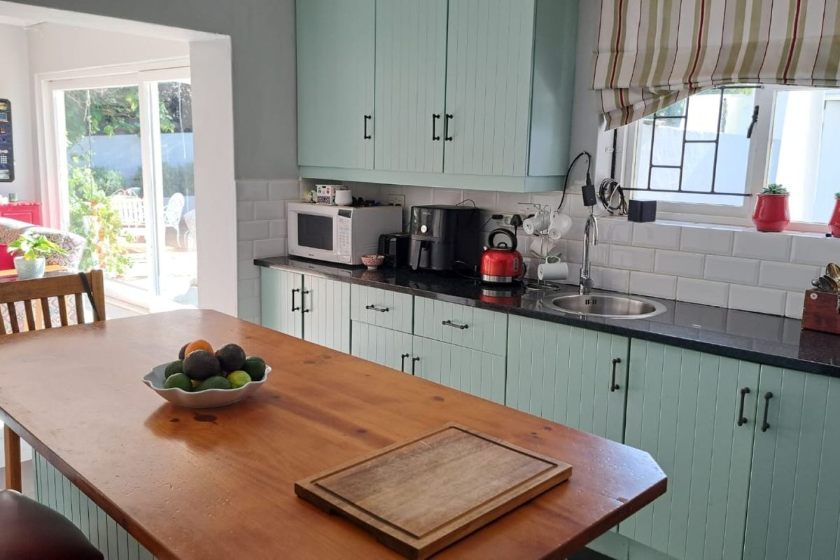 A functional kitchen featuring light green cabinetry, dark granite countertops, subway tile backsplash, and a wooden island, with direct access to the outdoor patio area.