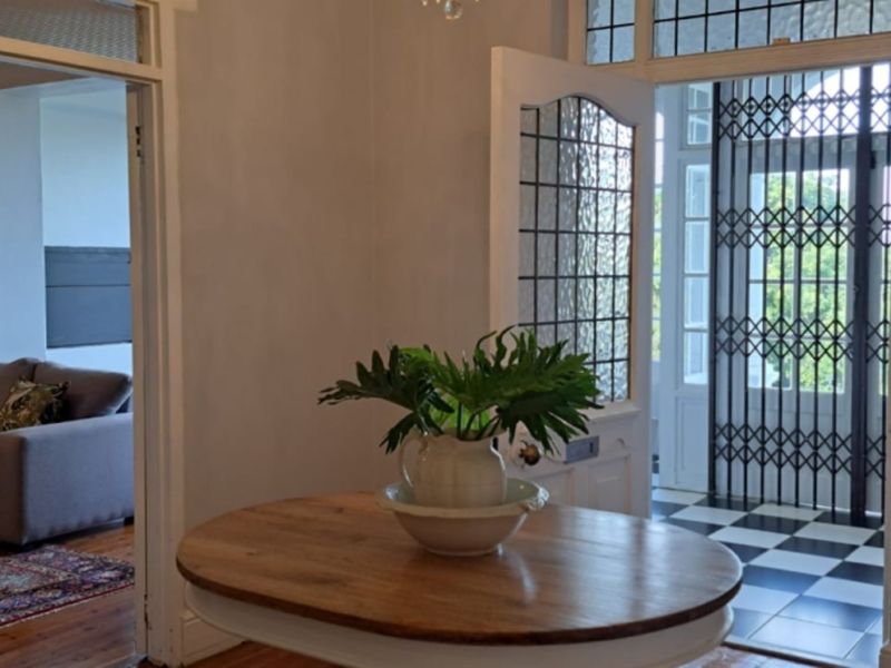 Welcoming entrance hall featuring classic checkered floor tiles, a leaded glass front door with security gate, and seamless flow into the adjacent living area.