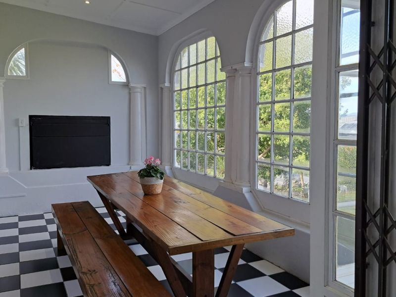 A bright, enclosed patio featuring classic checkered tile flooring, arched windows, decorative columns, and a built-in fireplace, offering a charming space for relaxation.