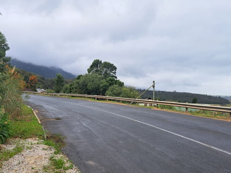 A view of the asphalt road and metal guardrail bordering the vacant land, featuring surrounding hills and natural landscape.