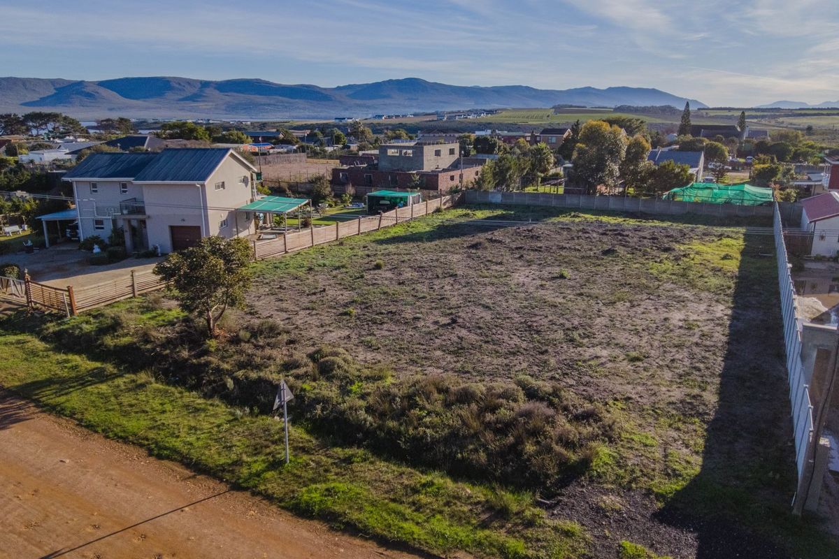 An aerial view of a vacant residential plot featuring perimeter fencing and boundary walls, situated in a developed neighborhood with mountain views.