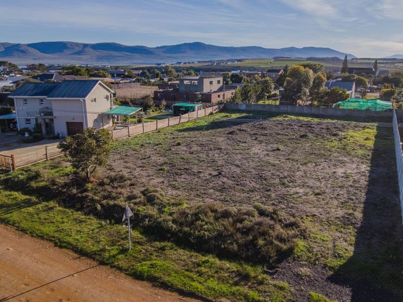 An aerial view of a vacant residential plot featuring perimeter fencing and boundary walls, situated in a developed neighborhood with mountain views.