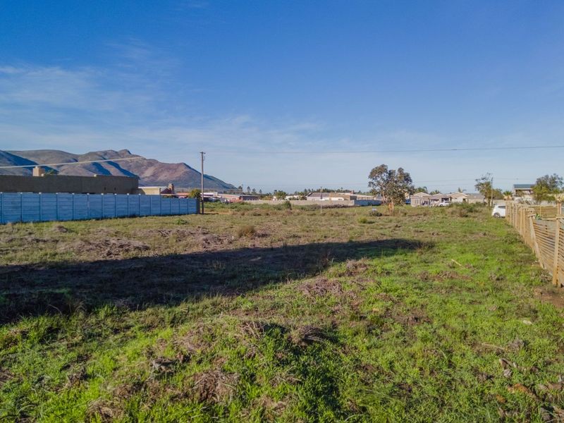 A vacant residential plot featuring a mix of precast concrete and timber boundary fencing with mountain views in the background.