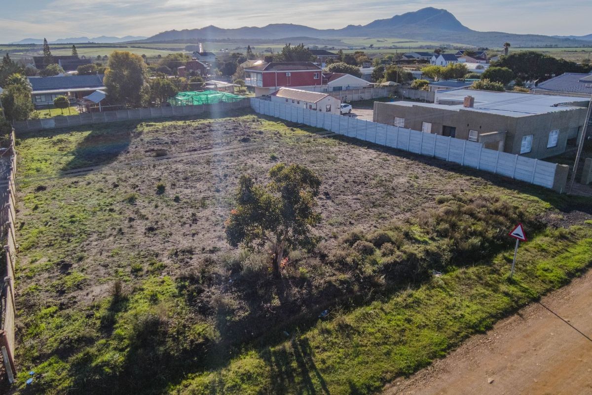 An aerial view of a vacant residential plot featuring a precast concrete boundary wall and mountain views in the background.