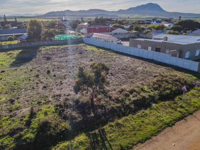 An aerial view of a vacant residential plot featuring a precast concrete boundary wall and mountain views in the background.