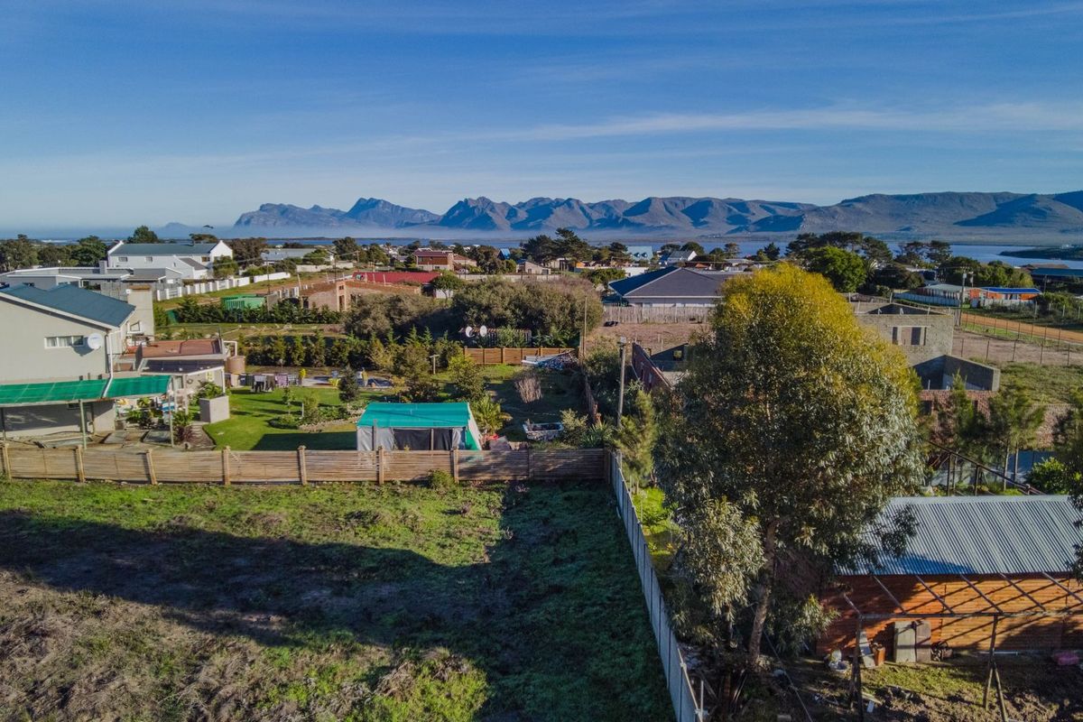 Aerial view of a residential vacant land plot featuring perimeter fencing, mature trees, and surrounding neighborhood views with mountains in the distance.