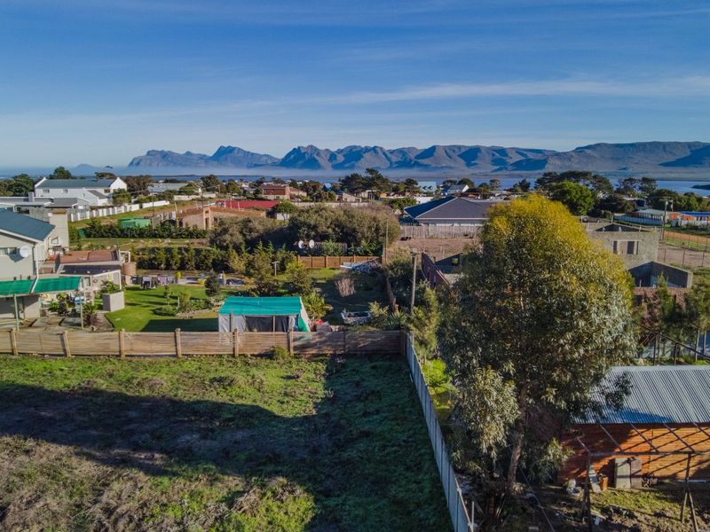 Aerial view of a residential vacant land plot featuring perimeter fencing, mature trees, and surrounding neighborhood views with mountains in the distance.