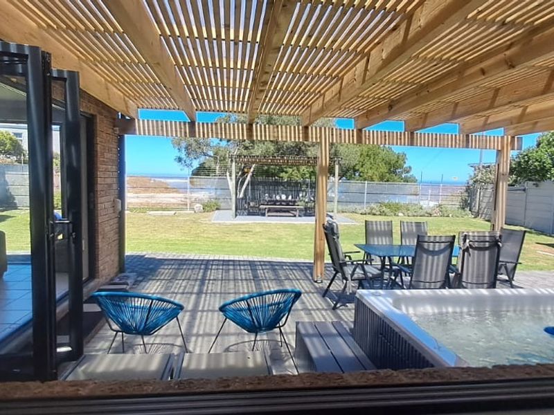 Covered outdoor patio featuring a timber pergola, built-in braai, and hot tub, overlooking a landscaped garden with sea views.