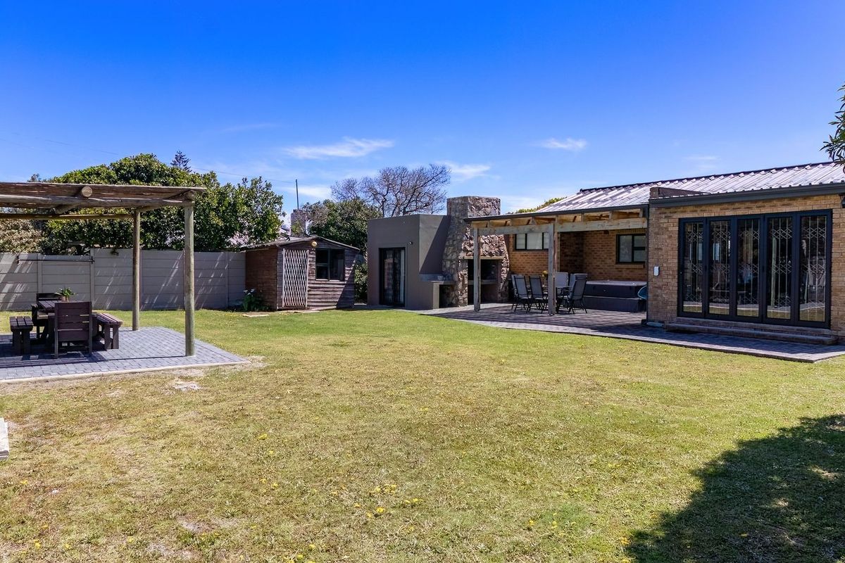 Spacious rear garden featuring a paved patio, built-in braai, pergola, and a well-maintained lawn with a storage shed.