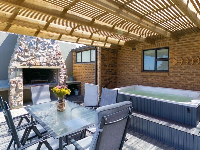 Covered outdoor patio featuring a stone-clad built-in braai, timber pergola overhead, and a built-in spa bath, perfect for relaxed outdoor entertaining.