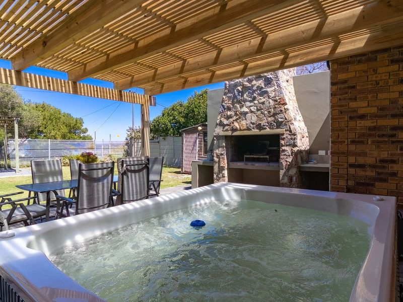 Covered outdoor patio featuring a wooden pergola, stone-clad built-in braai, and prep counter, overlooking a garden area.