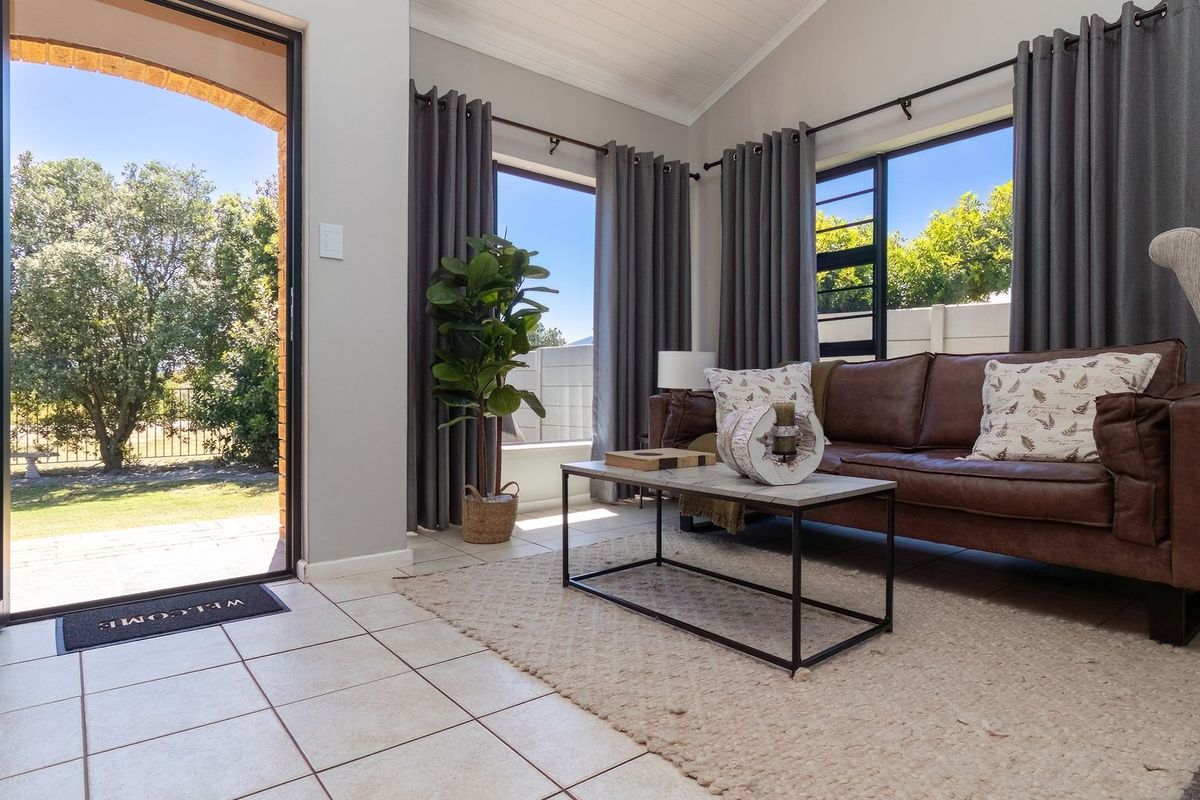 Bright living room featuring tiled flooring, a vaulted ceiling, and large windows with direct access to the outdoor garden area.