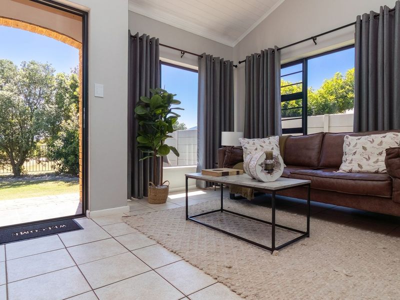 Bright living room featuring tiled flooring, a vaulted ceiling, and large windows with direct access to the outdoor garden area.