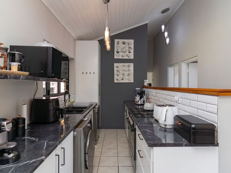 A modern galley-style kitchen featuring dark marble-effect countertops, white cabinetry, subway tile backsplash, and a high vaulted ceiling with pendant lighting.