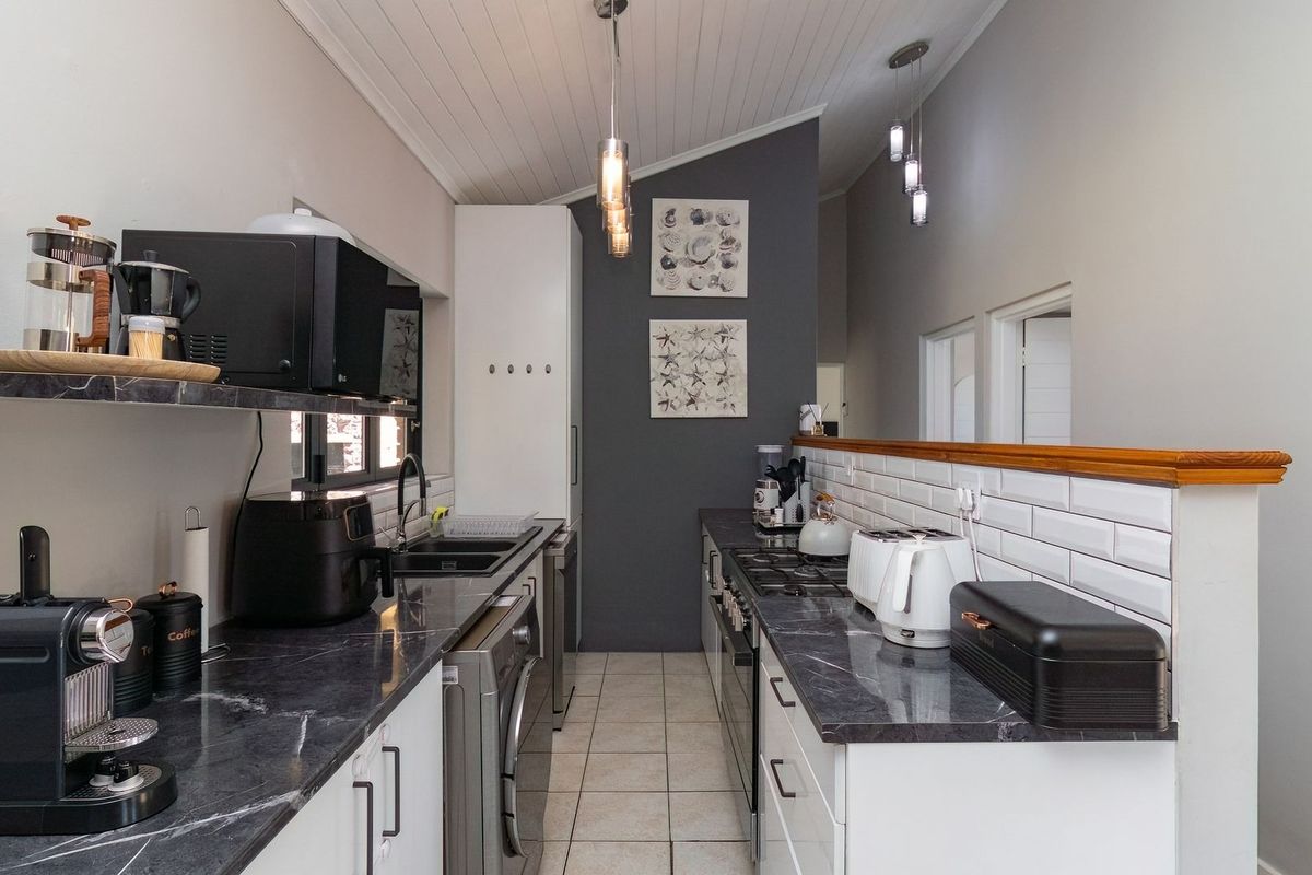 A modern galley-style kitchen featuring dark marble-effect countertops, white cabinetry, subway tile backsplash, and a high vaulted ceiling with pendant lighting.