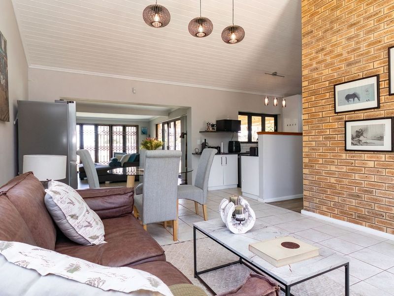 Spacious open-plan living and dining area featuring an exposed brick feature wall, tiled flooring, and a high tongue and groove ceiling with pendant lighting.