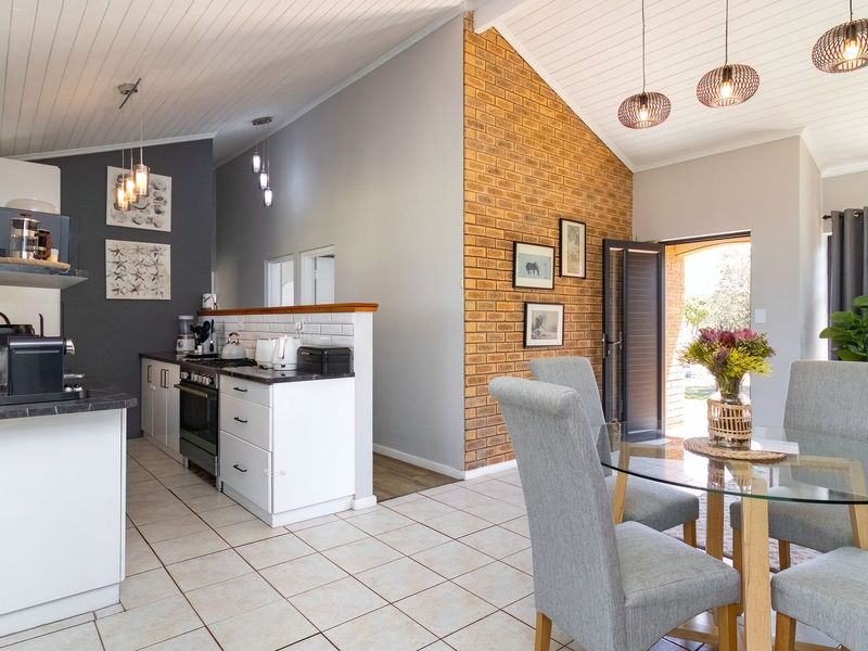 Open-plan living and kitchen area featuring a vaulted ceiling, exposed brick wall, tiled flooring, and modern kitchen cabinetry with a subway tile backsplash.