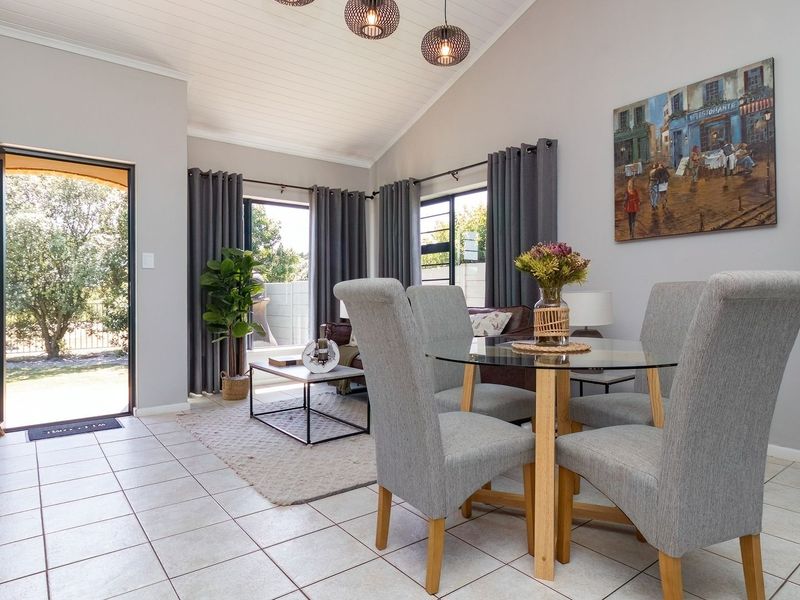 Bright open-plan living and dining area featuring vaulted ceilings, tiled floors, and an exposed brick feature wall with direct access to the garden.