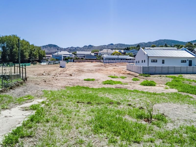 A vacant residential plot featuring cleared land, perimeter fencing, and a precast concrete boundary wall, situated in a developed neighborhood with mountain views.
