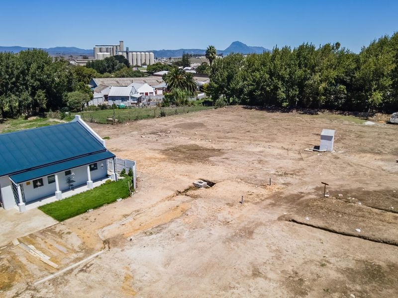 Aerial view of a large residential vacant land plot featuring an existing dwelling with a metal roof and garage, surrounded by mature trees.