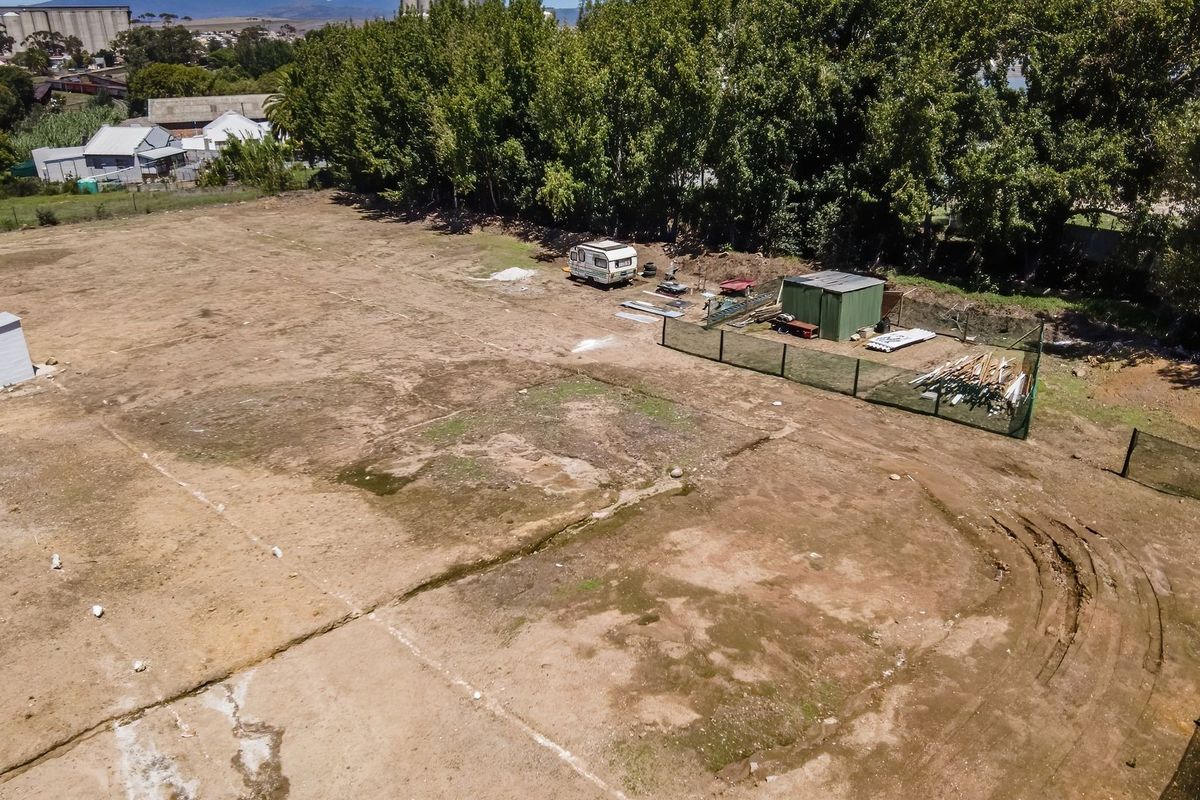 An aerial view of a vacant residential plot featuring perimeter fencing and a small utility structure, offering a clear perspective of the land.
