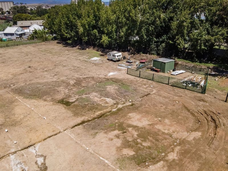 An aerial view of a vacant residential plot featuring perimeter fencing and a small utility structure, offering a clear perspective of the land.