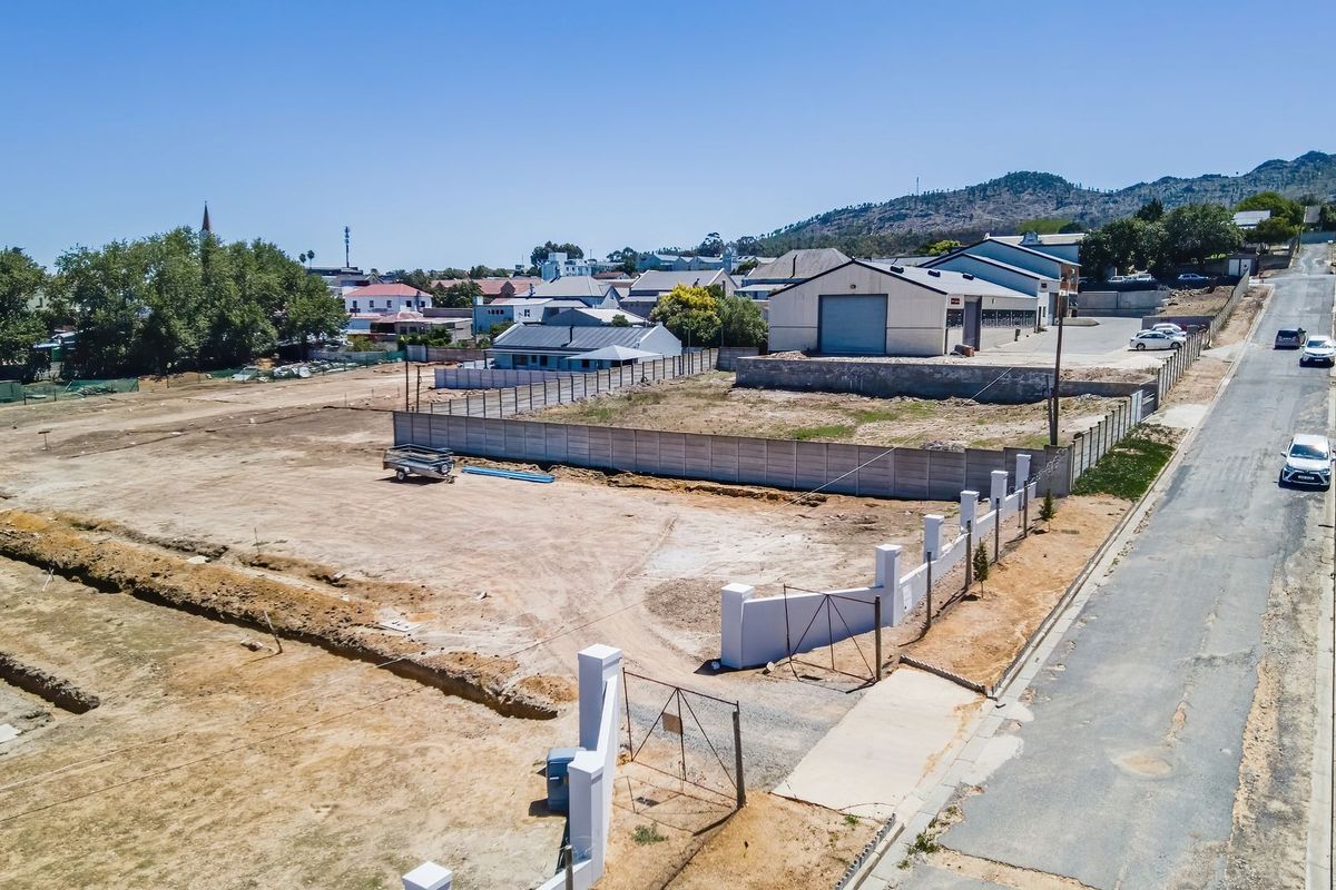 Aerial view of a vacant residential plot featuring perimeter fencing, a concrete boundary wall, and direct street access in a developed neighborhood.