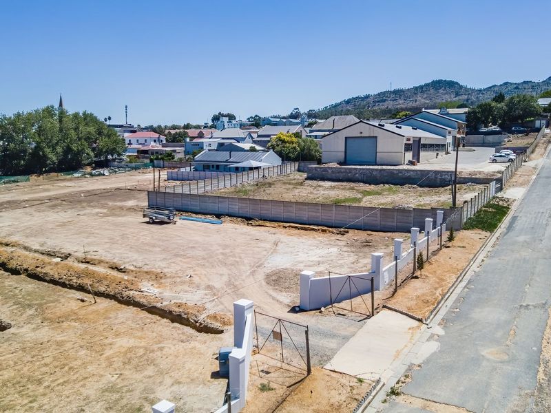 Aerial view of a vacant residential plot featuring perimeter fencing, a concrete boundary wall, and direct street access in a developed neighborhood.