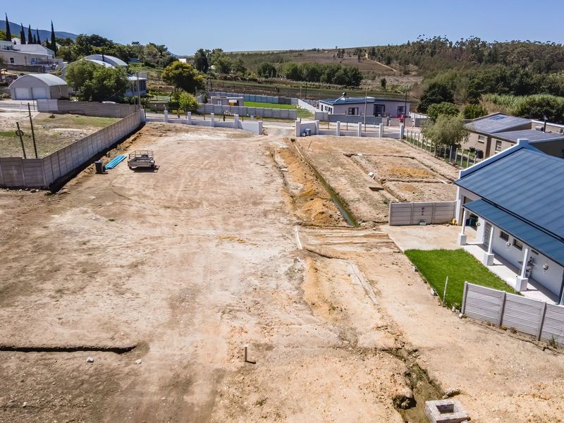 Aerial view of a cleared residential vacant plot featuring boundary walls and existing drainage infrastructure in a developed neighborhood.