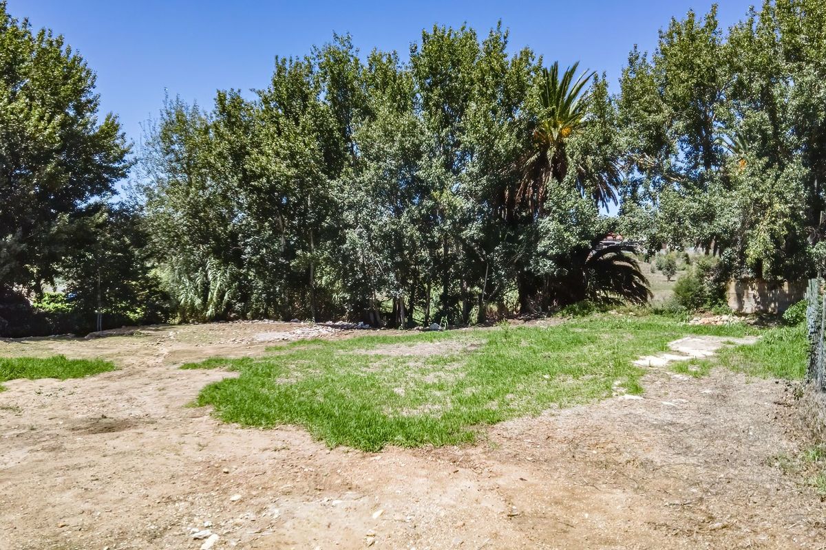 A vacant residential plot featuring natural grass, mature trees, and perimeter wire fencing, offering a clear space for potential development.