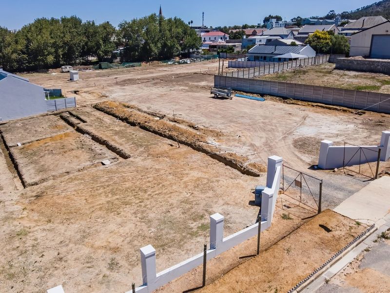 Aerial view of a vacant residential plot featuring perimeter walling, a gated entrance, and prepared foundation trenches ready for construction.