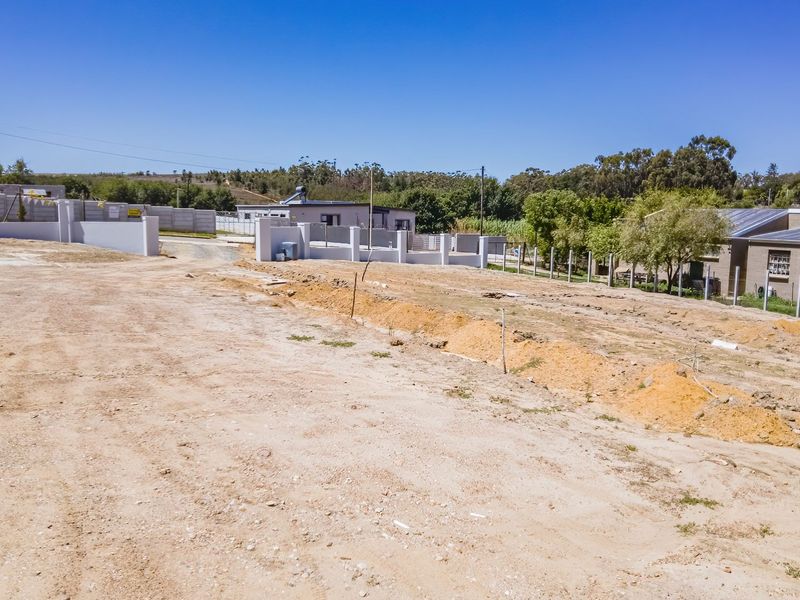 A vacant residential plot featuring cleared earth, boundary walls, and perimeter fencing, ready for development in a quiet neighborhood setting.