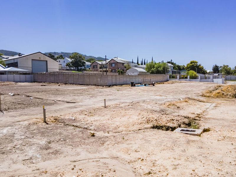 A vacant residential plot featuring a precast concrete boundary wall, utility service connections, and a stormwater drainage inlet, ready for development.