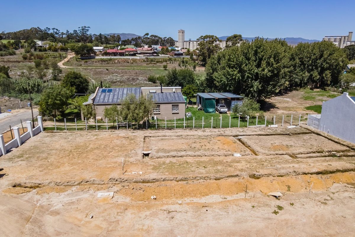 Aerial view of a vacant residential plot featuring excavated foundation trenches and perimeter fencing, situated in a developing neighborhood.