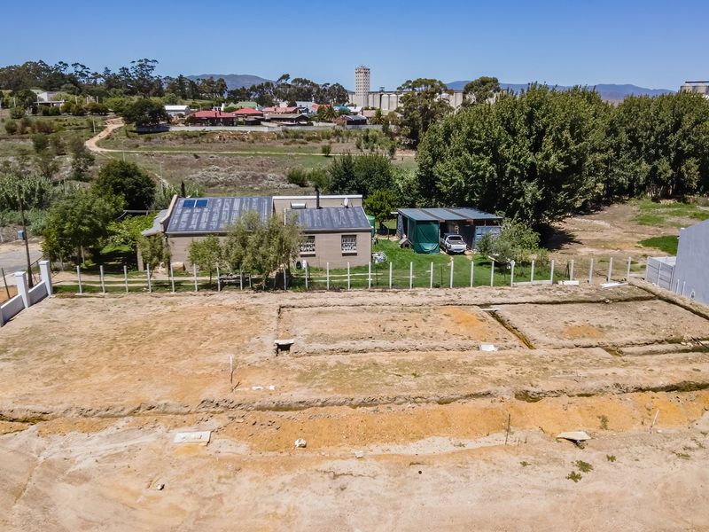 Aerial view of a vacant residential plot featuring excavated foundation trenches and perimeter fencing, situated in a developing neighborhood.