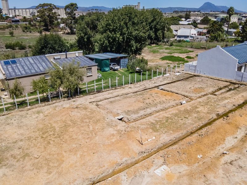 Aerial view of a vacant residential plot featuring excavated foundation trenches and perimeter fencing, situated in a developing neighborhood.