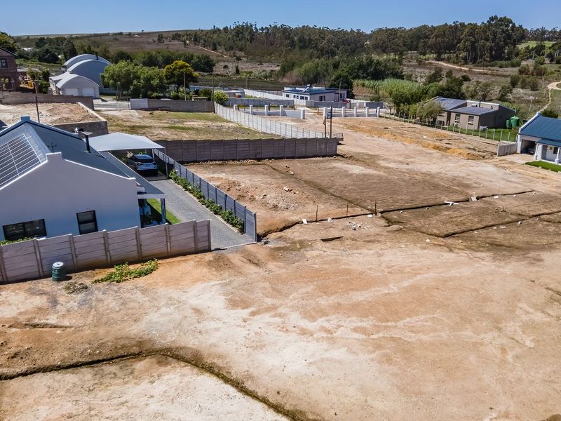 Aerial view of a vacant residential plot featuring surrounding boundary walls and adjacent established housing in a developing estate.
