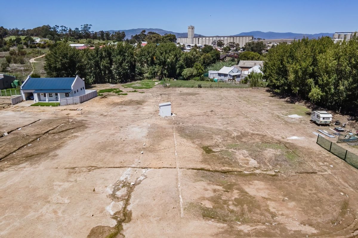 An aerial view of a vacant residential plot featuring open land, perimeter fencing, and a central utility connection point.
