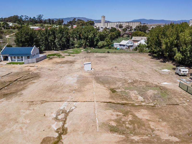 An aerial view of a vacant residential plot featuring open land, perimeter fencing, and a central utility connection point.