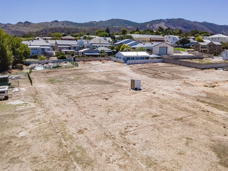 An aerial view of a vacant residential plot featuring boundary walls and perimeter fencing, situated in a developed neighborhood with mountain views.