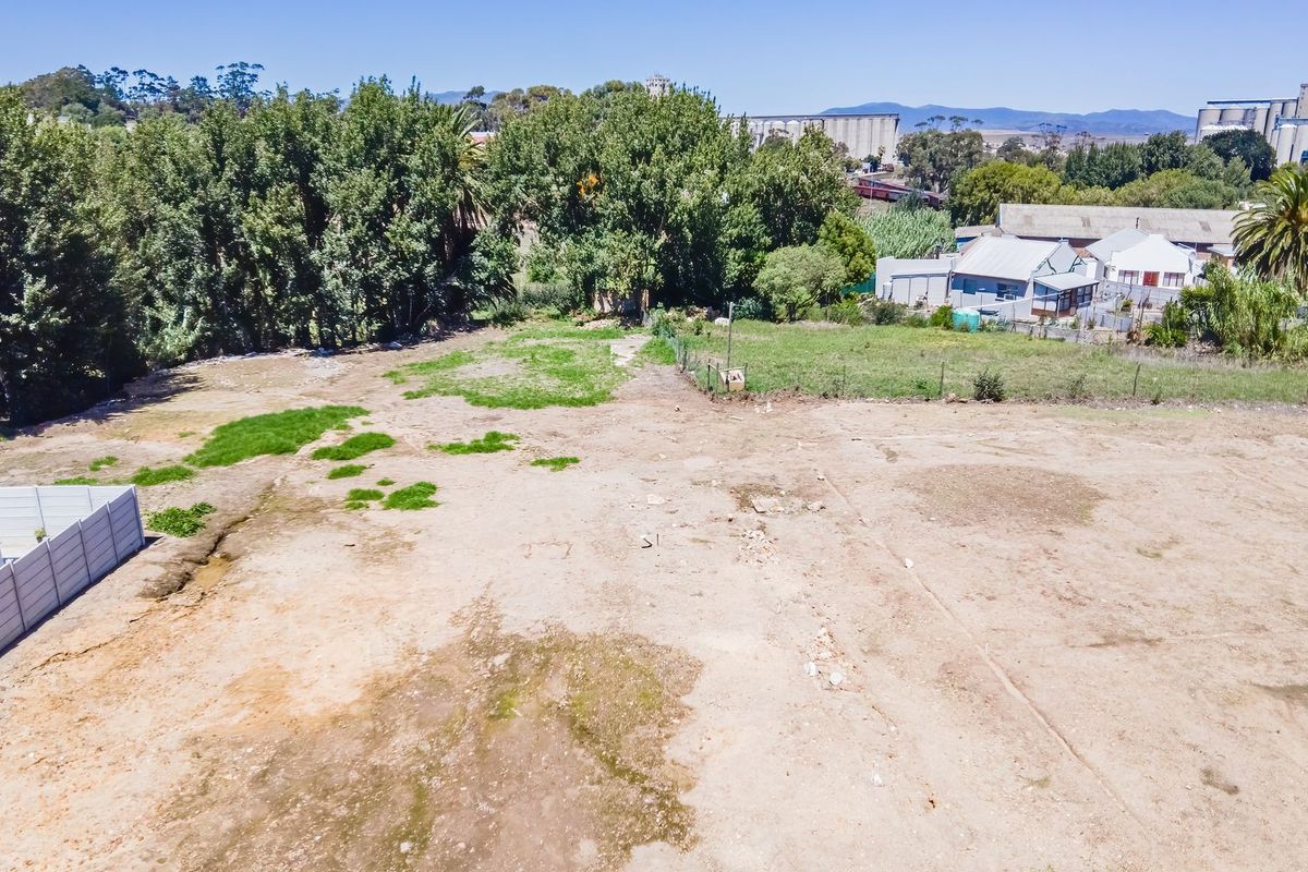 An aerial view of a vacant residential plot featuring open land, perimeter fencing, and established trees in the surrounding area.