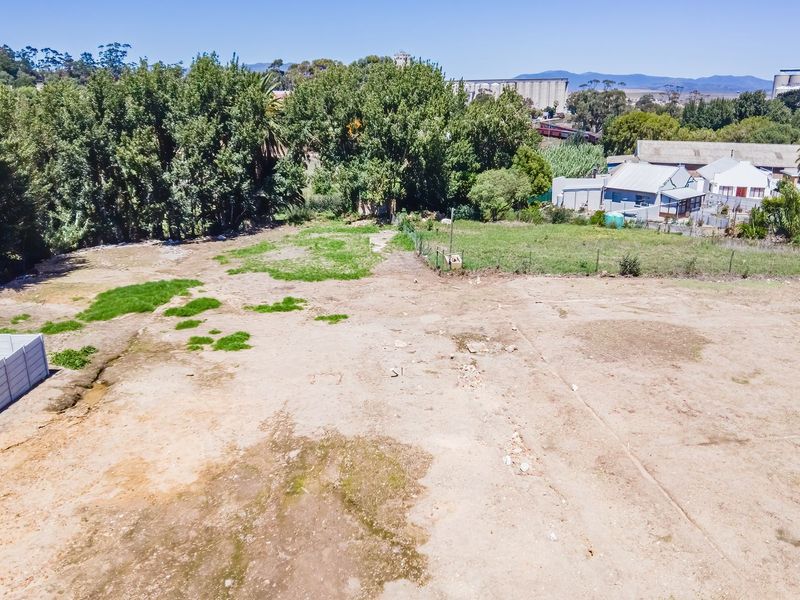 An aerial view of a vacant residential plot featuring open land, perimeter fencing, and established trees in the surrounding area.