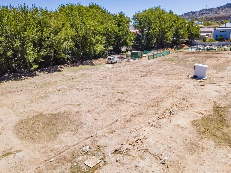 An elevated aerial view of a vacant residential plot featuring cleared land, perimeter fencing, and mature trees along the boundary.