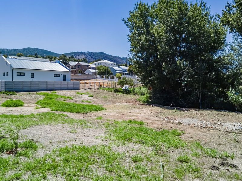 A view of a vacant residential plot featuring natural terrain and a precast concrete boundary wall bordering the adjacent property.