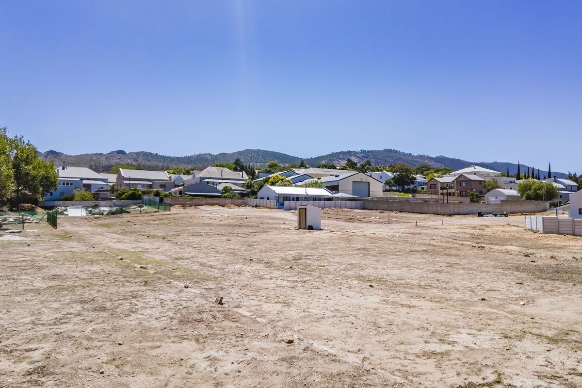 A vacant residential plot of land featuring a level surface, perimeter fencing, and a precast concrete boundary wall with mountain views in the background.