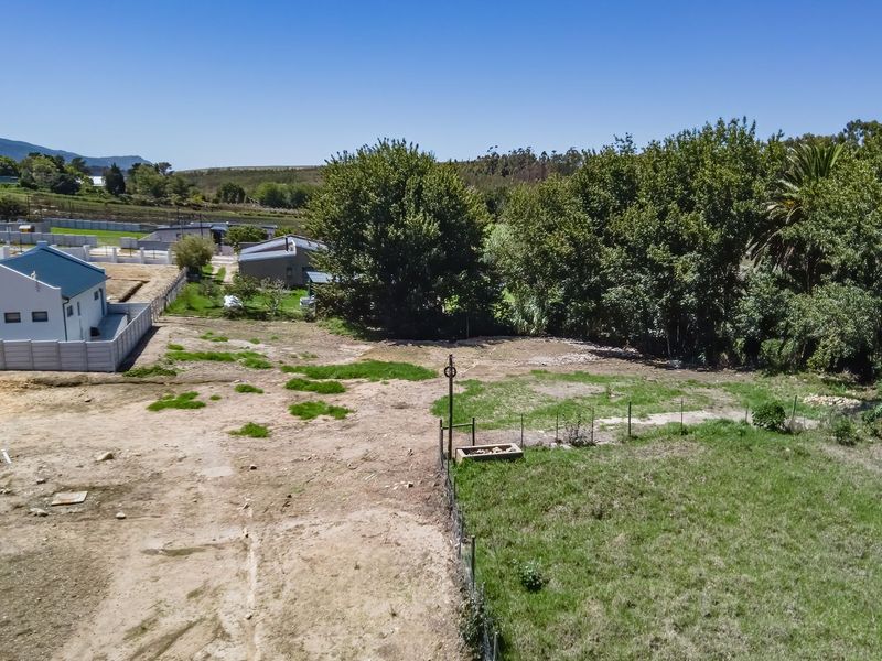 An aerial view of a vacant residential plot featuring cleared land, perimeter fencing, and established trees in a quiet neighborhood setting.